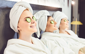 Three women in white robes and towels wrapped around their hair relaxing at spa with cucumber slices on their eyes 