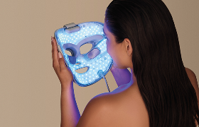 Woman holding Shark CryoGlow in front of her face, illuminated with blue light therapy, preparing to apply device for at-home skin treatment and rejuvenation 