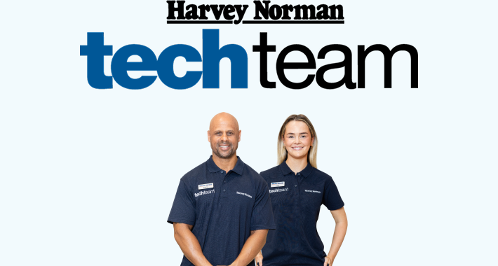 Two Harvey Norman Tech Team staff members wearing branded uniforms standing in front of the Harvey Norman Tech Team logo.