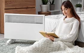 Woman reading beside a white panel heater in a bedroom setting