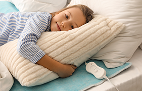 Young girl smiling while resting on a heated electric blanket with remote