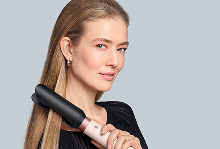 Woman with long straight hair holding a sleek hair straightener styling tool from Dyson