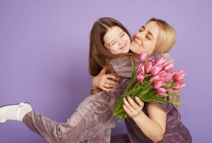 Happy mother receiving bouquet of pink tulips from daughter on purple background