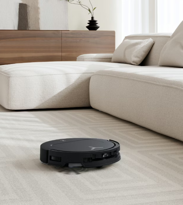 Black robot vacuum cleaner navigating beige carpet in modern living room