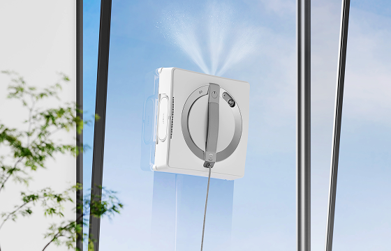 Robot window cleaner spraying cleaning solution across a tall floor-to-ceiling glass window