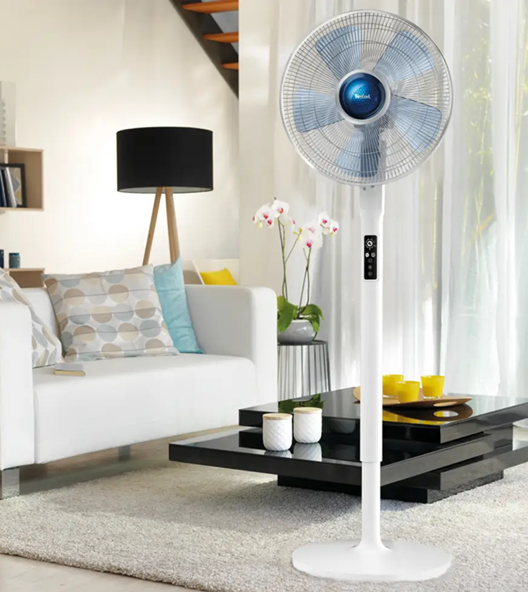 Tefal Turbo Silence Extreme White Pedestal Fan with blue blades and control panel in bright living room beside white sofa, orchid plant and black coffee table 