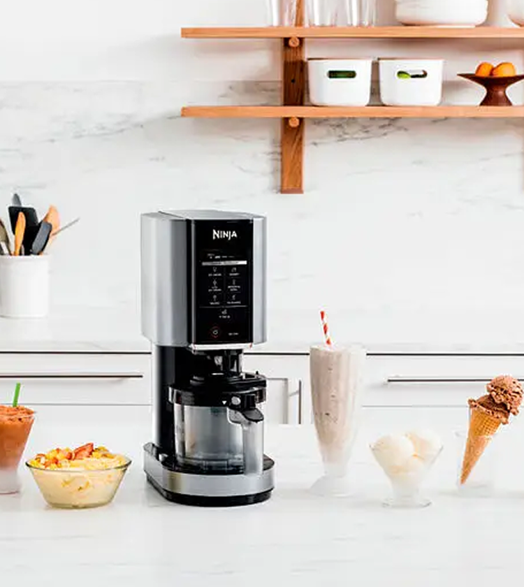 Ninja CREAMi sitting on a modern kitchen bench with milkshakes, frozen desserts and ice cream cones. 