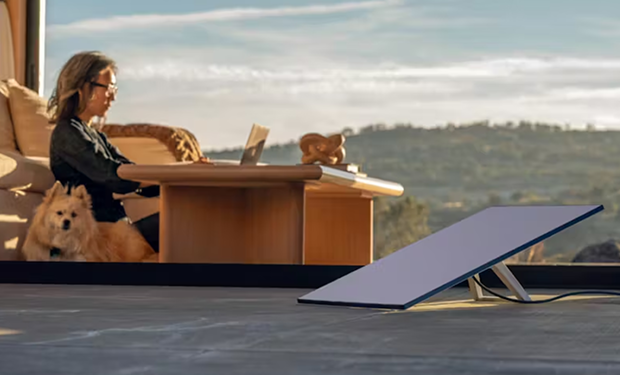 Starlink satellite dish set up outside modern home with woman working on laptop indoors at a coffee table beside her dog