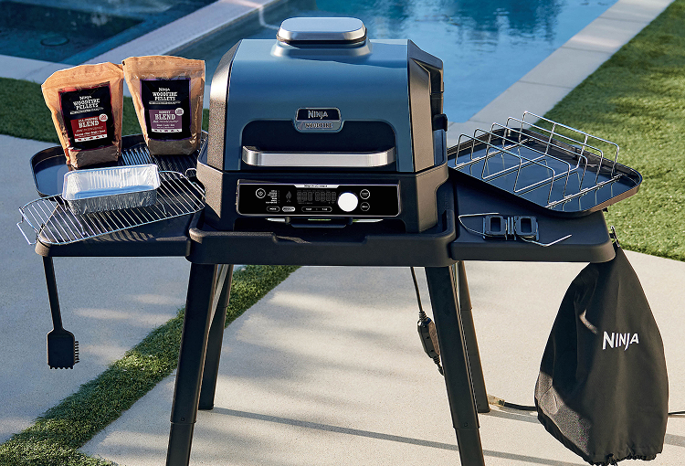 Ninja Woodfire outdoor BBQ with grill racks, trays, tools and woodfire pellets beside a swimming pool