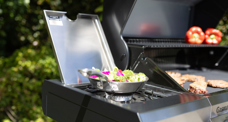 asmate gas BBQ with side burner cooking vegetables beside grilled steaks 