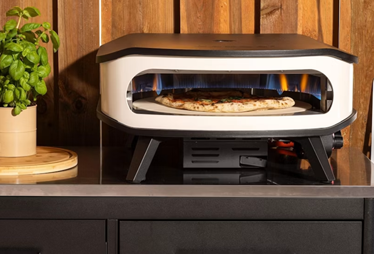 Outdoor pizza oven cooking a pizza over an open flame on a benchtop 